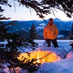 man standing in snow while enjoying campfire