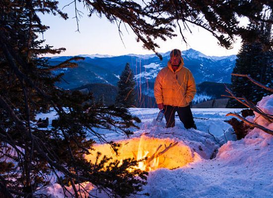 man standing in snow while enjoying campfire