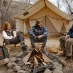 friends enjoying campfire at with beautiful wall tent setup behind for camping