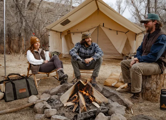 friends enjoying campfire at with beautiful wall tent setup behind for camping