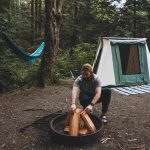 man setting up campfire for long term camping with canvas tent