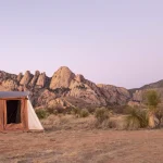 Outdoor photograph featuring a tent in the desert, framed by distant mountains under a clear sky