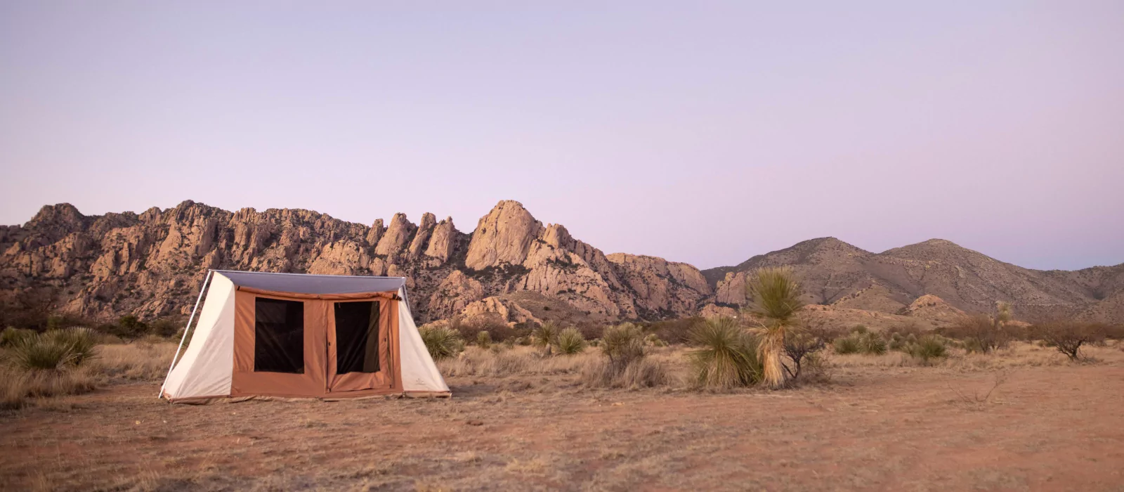 Outdoor photograph featuring a tent in the desert, framed by distant mountains under a clear sky