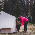 girl enjoying outdoors with her dog and camping in small 2 person tent in the forest