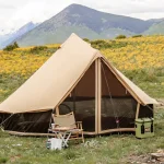 yurt tent setup in plain green field surrounded by mountains