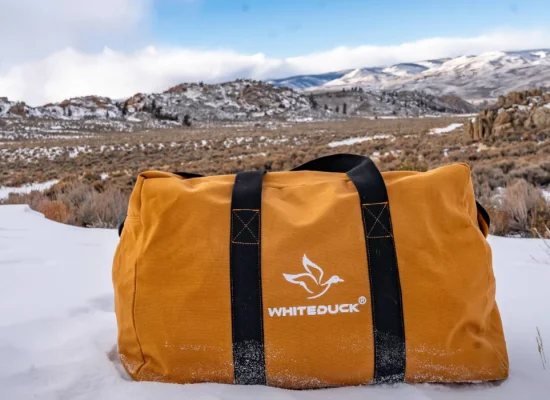 orange canvas bag on snow covered ground with a mountainous landscape and cloudy sky in the background