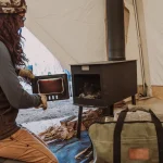 Camper setting up a wood-burning tent stove inside a canvas tent