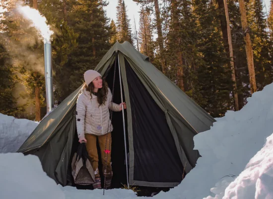 Woman enjoying winter camping in a snowy forest with a heated tent.