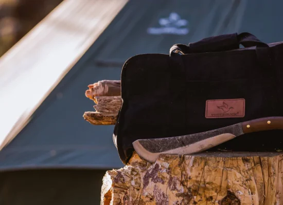 A durable log carrier bag from White Duck, filled with firewood, resting on a stump next to a camping tent and an axe