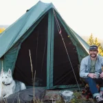 man sitting with his dog in front of canvas tent during wildlife camping