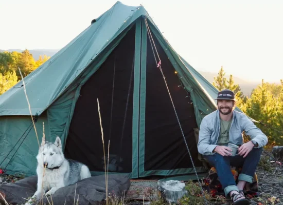 man sitting with his dog in front of canvas tent during wildlife camping