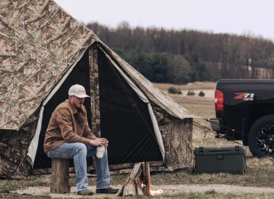 A man sits on a bench beside a tent alone, enjoying the outdoors in a serene natural setting