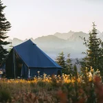 canvas tent setup in green fields with mountains behind for off season camping