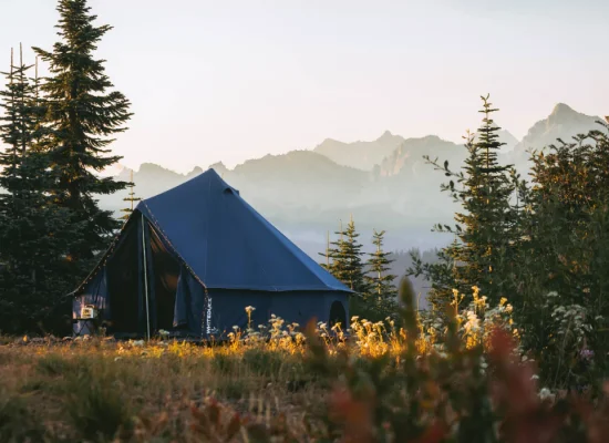 canvas tent setup in green fields with mountains behind for off season camping