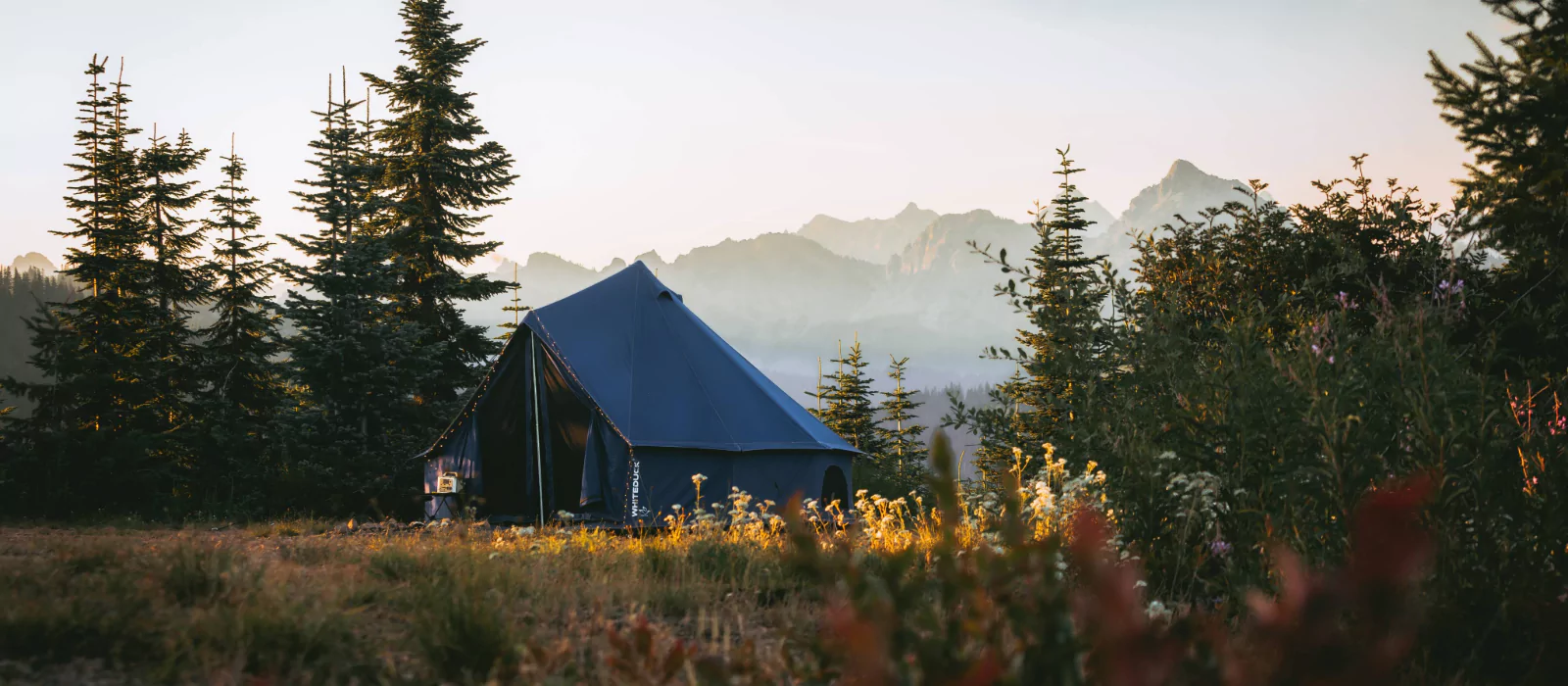 canvas tent setup in green fields with mountains behind for off season camping