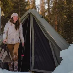 girl coming out from canvas tent with stove setup in snow for winter camping