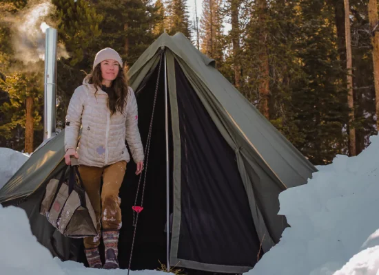 girl coming out from canvas tent with stove setup in snow for winter camping