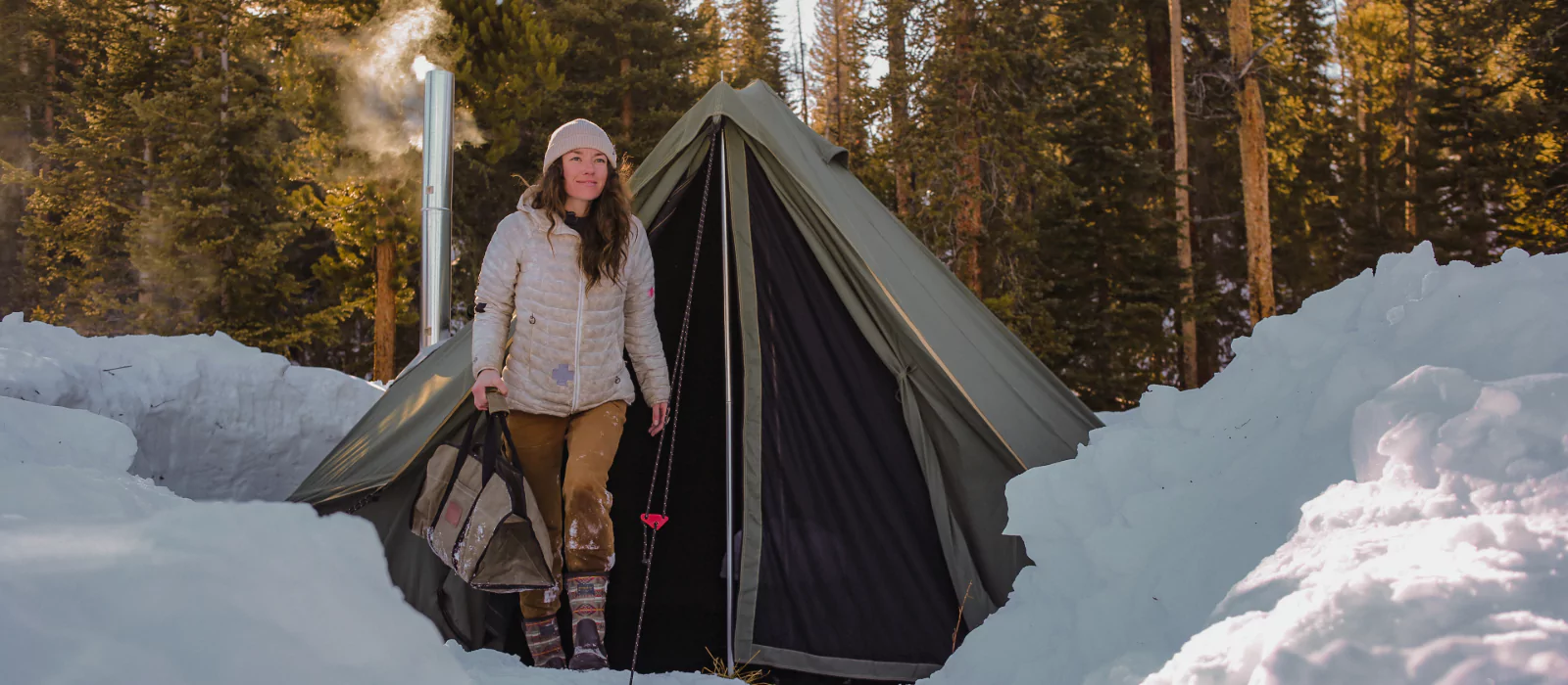 girl coming out from canvas tent with stove setup in snow for winter camping