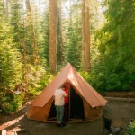 Camping tent set up in a scenic outdoor destination surrounded by lush green forest, perfect for nature and adventure enthusiasts.