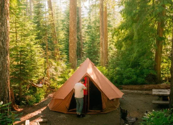Camping tent set up in a scenic outdoor destination surrounded by lush green forest, perfect for nature and adventure enthusiasts.