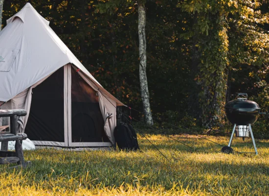 Spacious four-season tent set up in a scenic outdoor campsite, surrounded by lush greenery and camping essentials.