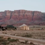 Overlanding setup in a remote desert with a canvas tent, off-road truck, and rugged landscape, perfect for adventure travel.