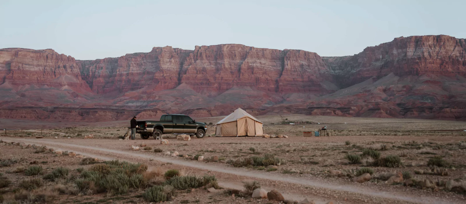 Overlanding setup in a remote desert with a canvas tent, off-road truck, and rugged landscape, perfect for adventure travel.