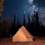Cozy tent setup under a star-filled night sky, perfect for stargazing in the wilderness.