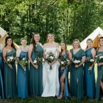 Bride and bridesmaids posing outdoors at a glamping-style camp wedding venue in the USA, surrounded by tents and forest scenery.