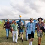 Group of friends walking through a colorful tent campsite at a California camping music festival, enjoying summer vibes and live music.