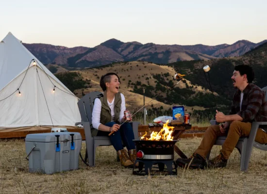 Couple cooking at camp with a fire pit and glamping tent in the mountains