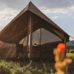 Canvas tent set up in a grassy field during early spring at sunset, perfect for seasonal camping