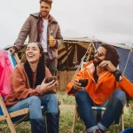 Friends relaxing with drinks outside tents at a music festival camping site
