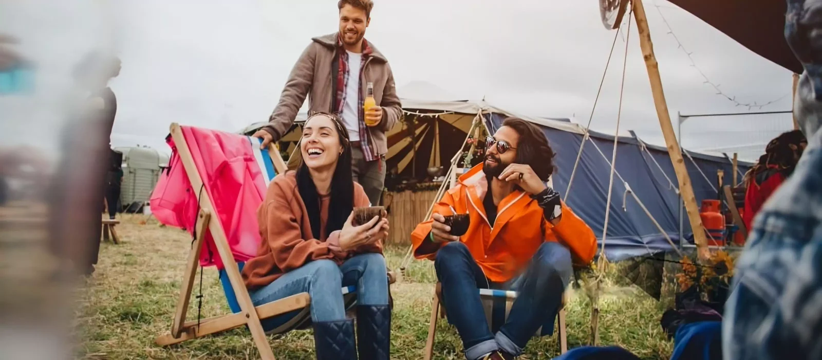 Friends relaxing with drinks outside tents at a music festival camping site