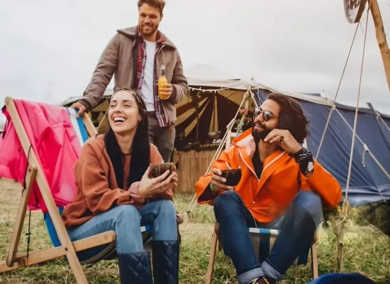 Friends relaxing with drinks outside tents at a music festival camping site
