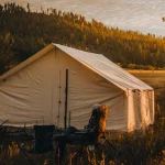 Group camping near military surplus tent in forest clearing at golden hour