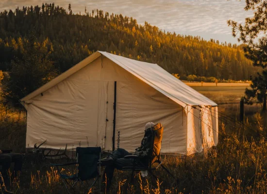 Group camping near military surplus tent in forest clearing at golden hour