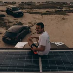 Camper enjoying off-grid beach camping with solar panels on van roof during a solar-powered camping trip.