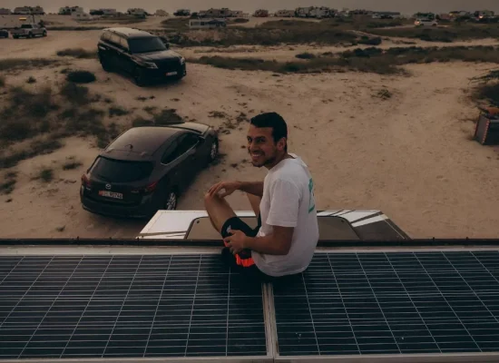 Camper enjoying off-grid beach camping with solar panels on van roof during a solar-powered camping trip.