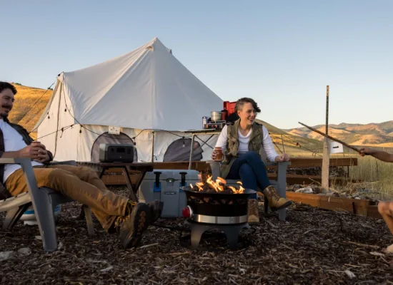 A family enjoying spring camping with kids around a campfire in front of a canvas tent in the mountains.