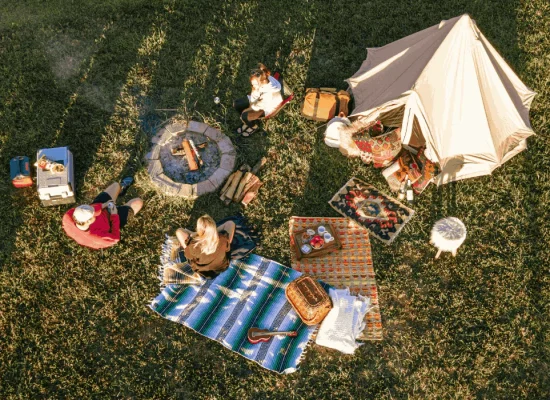 Campers enjoying a camp meal around a fire pit with tent and cooking setup on grassy field