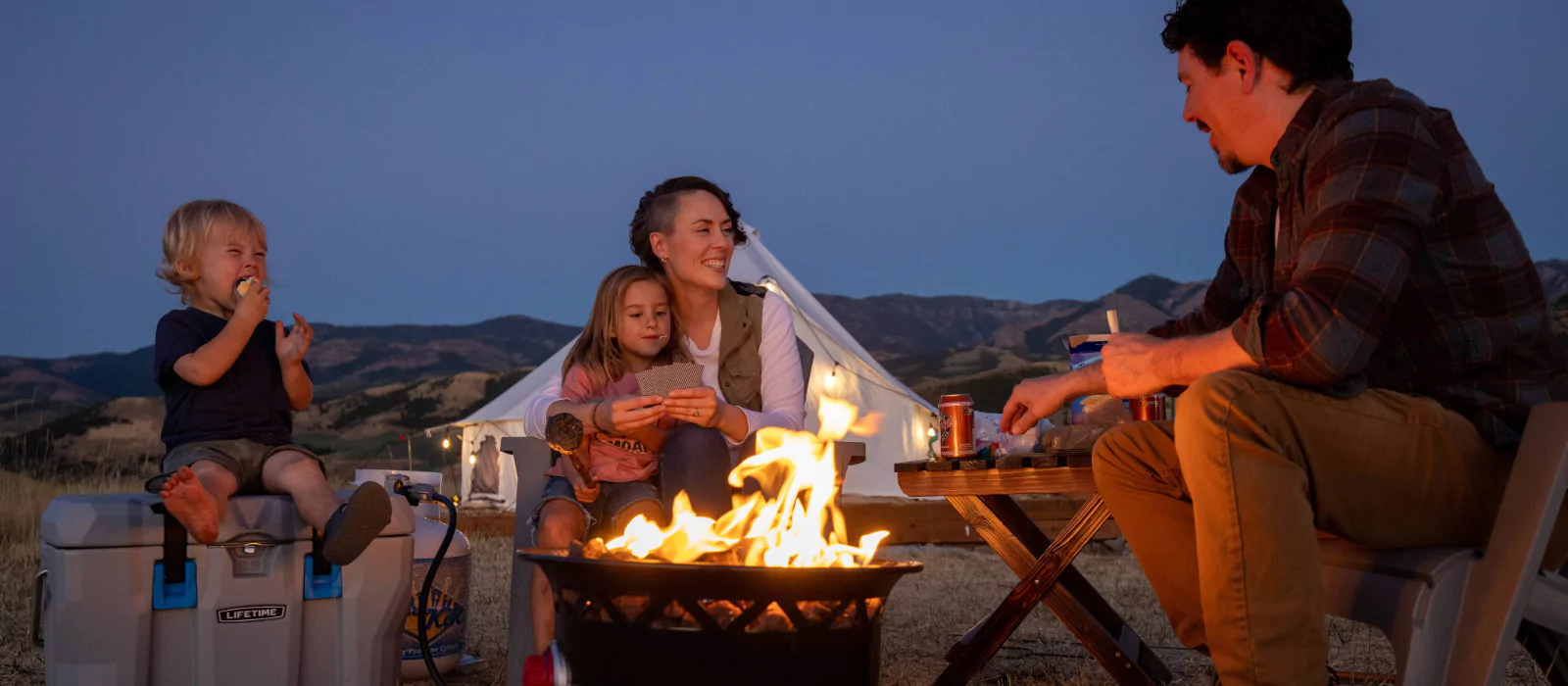 Family camping at a national park with kids around a campfire at dusk