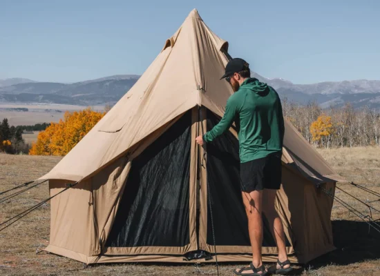Man setting up a canvas tent in a quiet, crowd-free national park with fall foliage and mountain views
