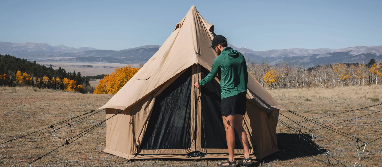 Man setting up a canvas tent in a quiet, crowd-free national park with fall foliage and mountain views