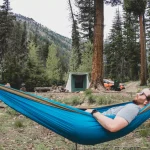 Man relaxing in a hammock at a forest campsite practicing camping for self-care