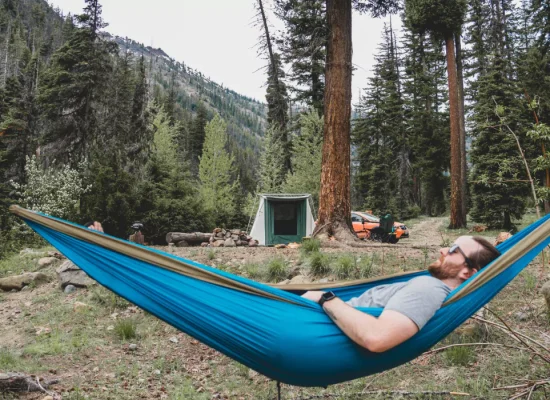 Man relaxing in a hammock at a forest campsite practicing camping for self-care