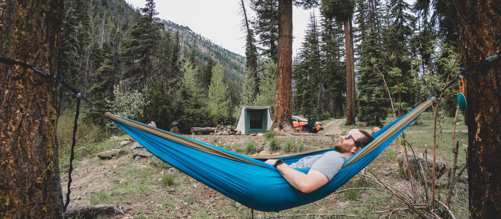 Man relaxing in a hammock at a forest campsite practicing camping for self-care
