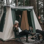 Campers dealing with common camping issues outside a canvas tent in the forest