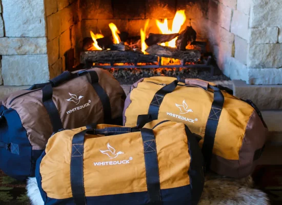 Durable canvas duffel bags perfect for camping and travel near a cozy fireplace