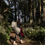 Person hiking through a forest trail carrying camping gear